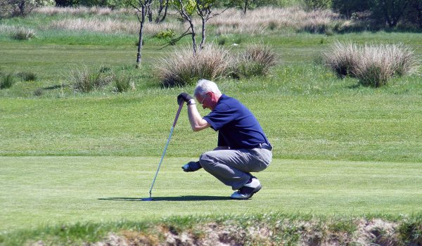 man crouched down looking at golf ball